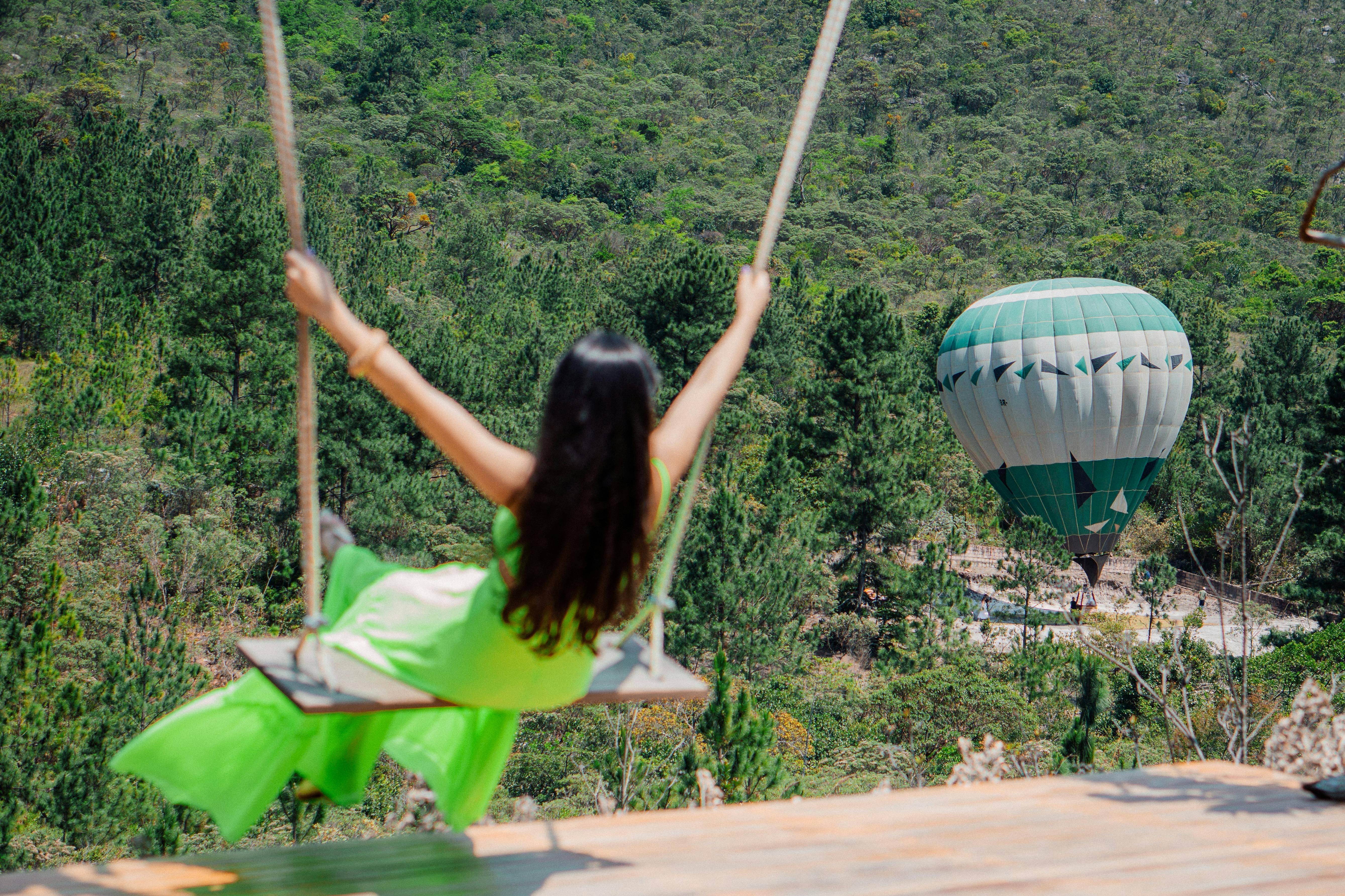 Bali — A woman in a green dress swinging above a forest with a hot air balloon in the background.