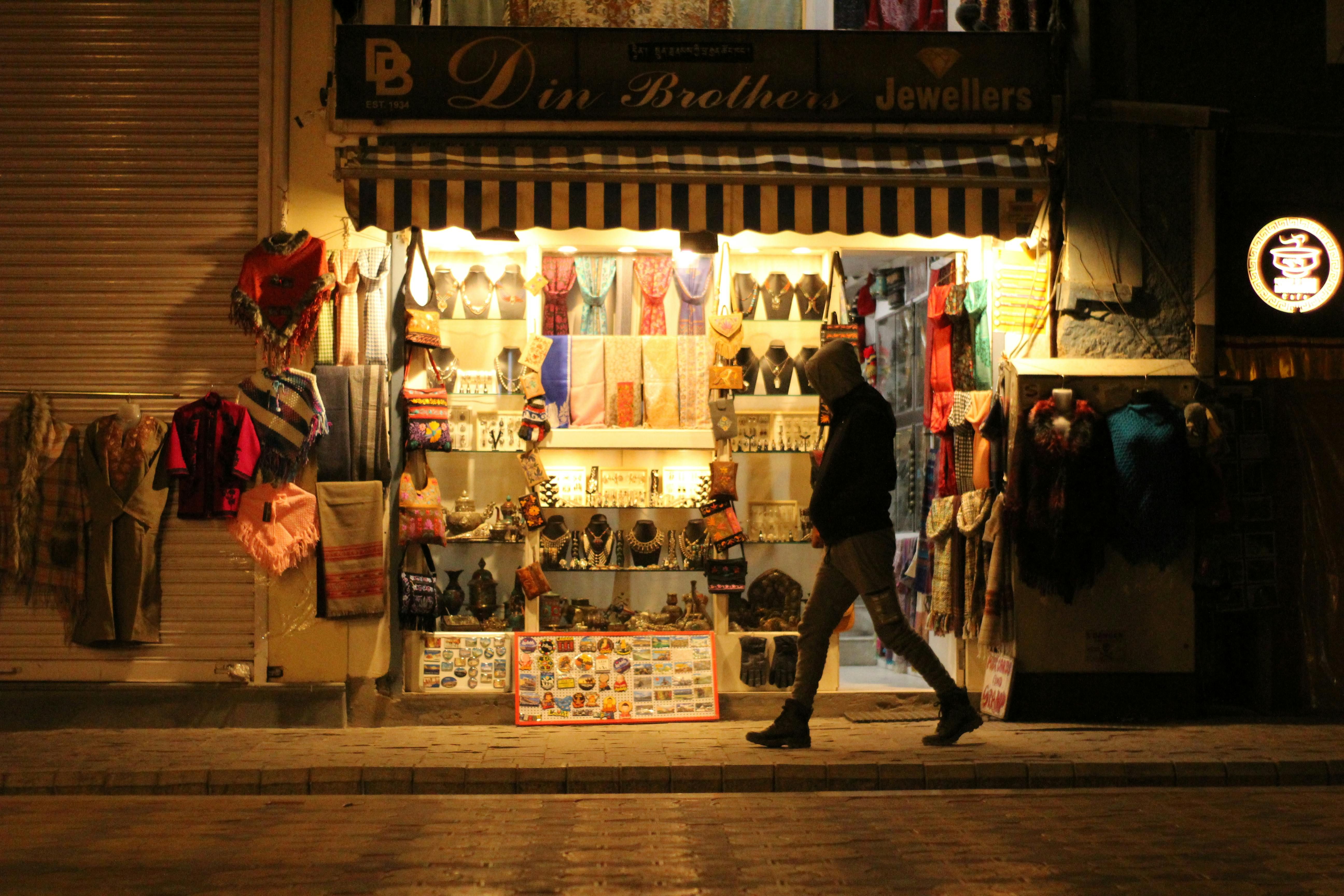 Bali — A person walks past an illuminated jewelry store on a city street at night.