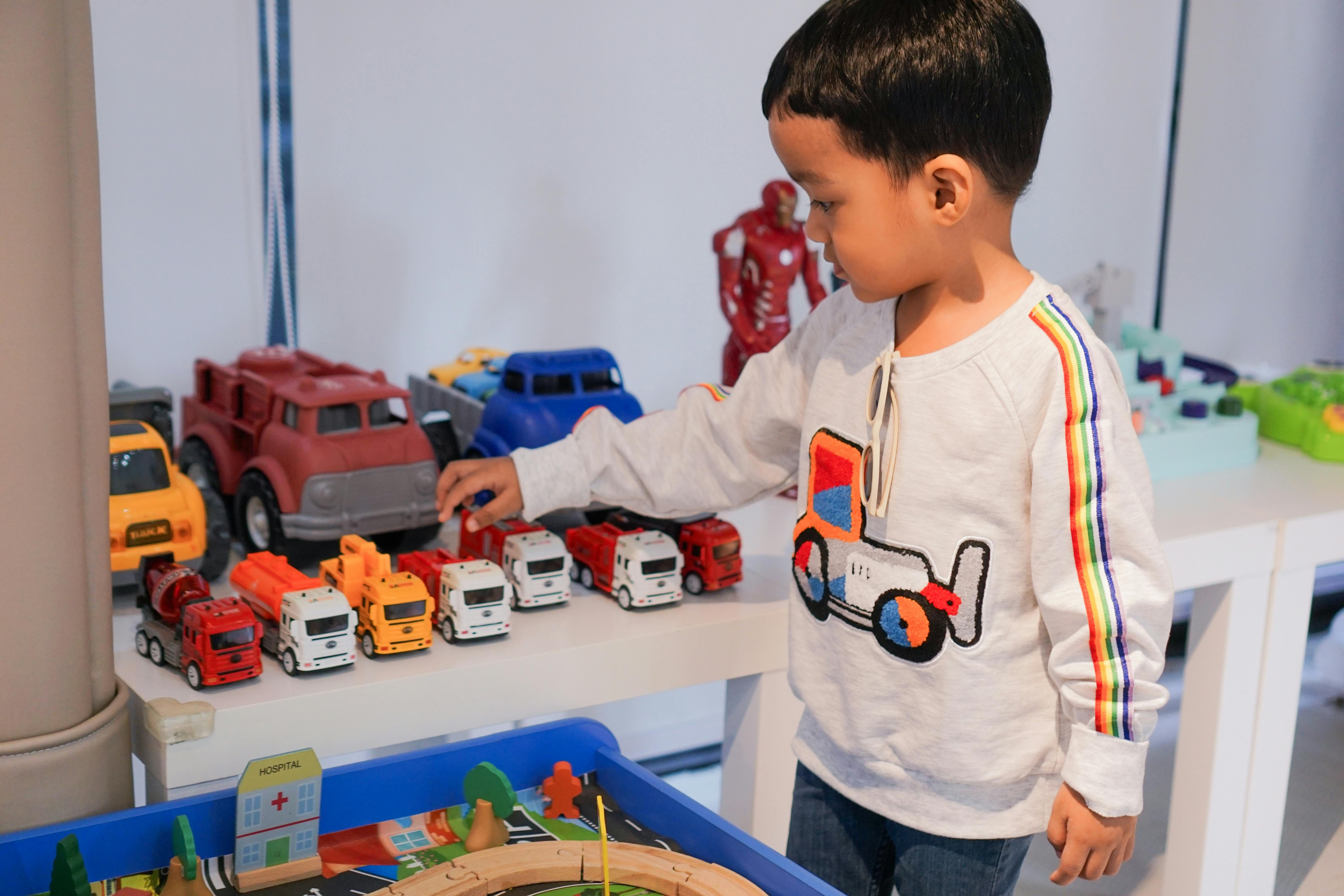 Bali — A young boy playing indoors with colorful toy trucks on a table, focused and imaginative.