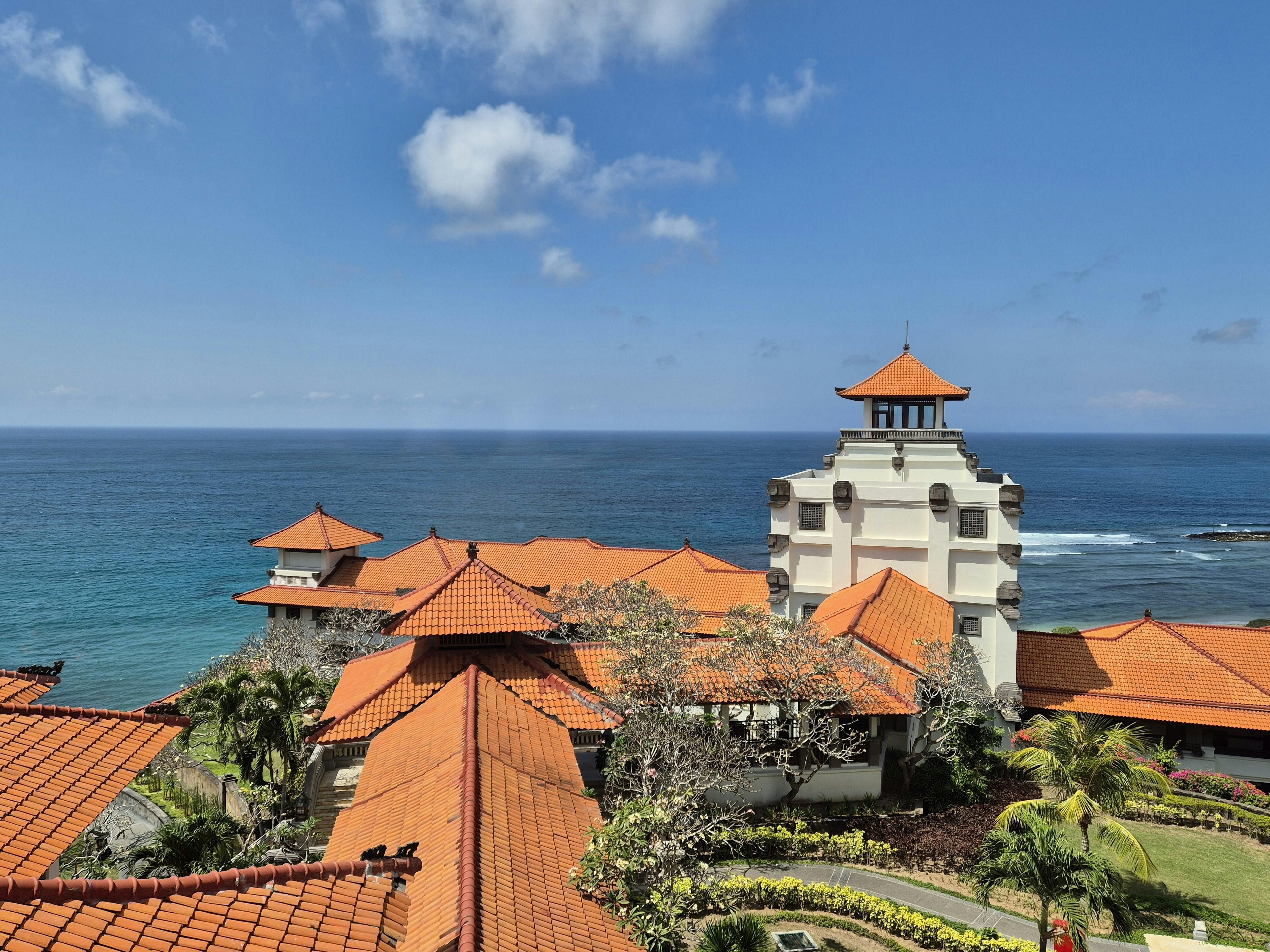Bali — A stunning view of a traditional Bali resort with red roofs overlooking the blue ocean under a clear sky.