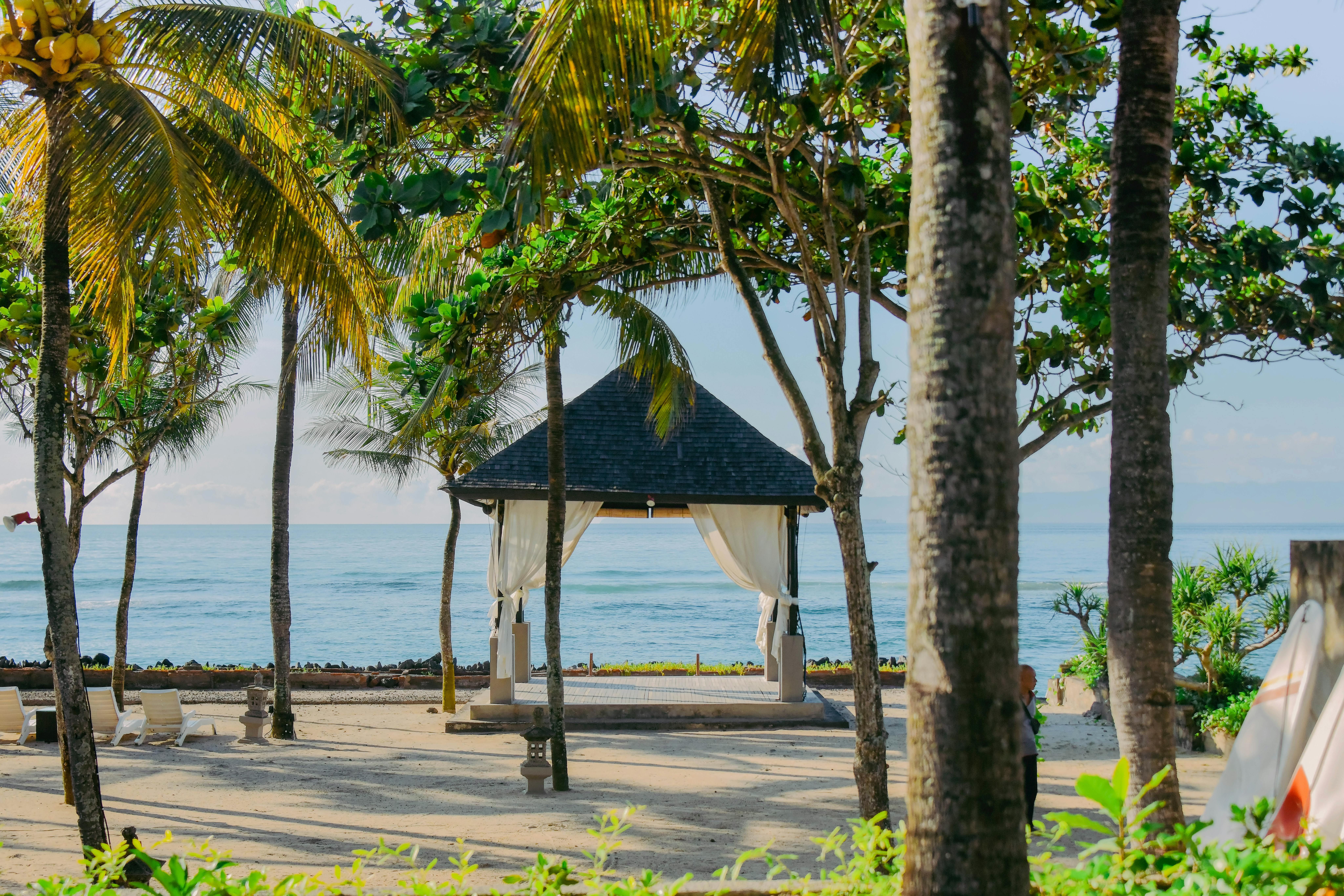 Bali — Tropical pavilion with palm trees by the beach in Bali, Indonesia, offering a serene coastal view.