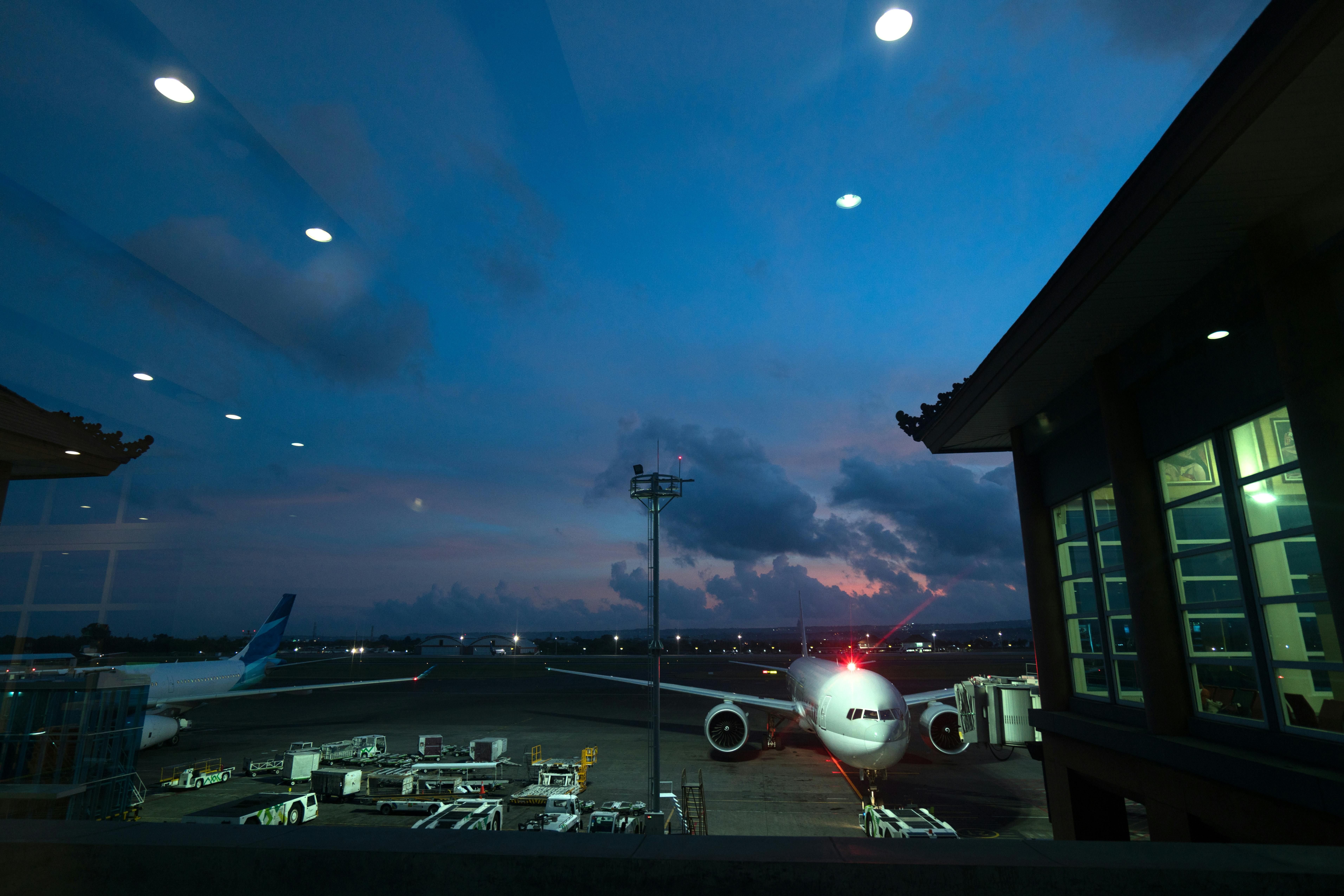 Bali — Contemporary airplanes with red beacon parked on airfield near airport service vehicles and terminal at night