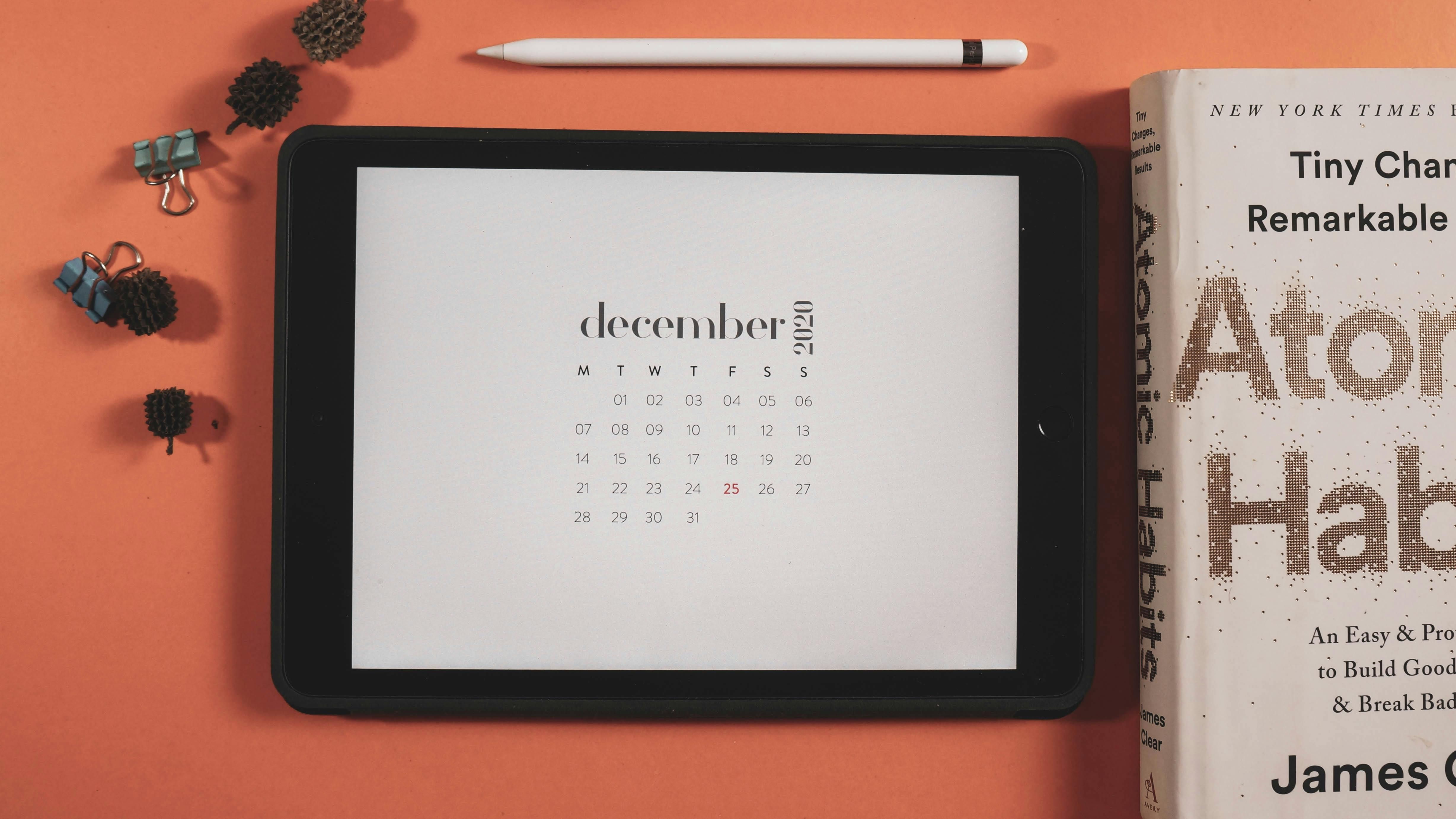 Bali — Minimalist flat lay featuring a tablet displaying a December 2020 calendar and a book.