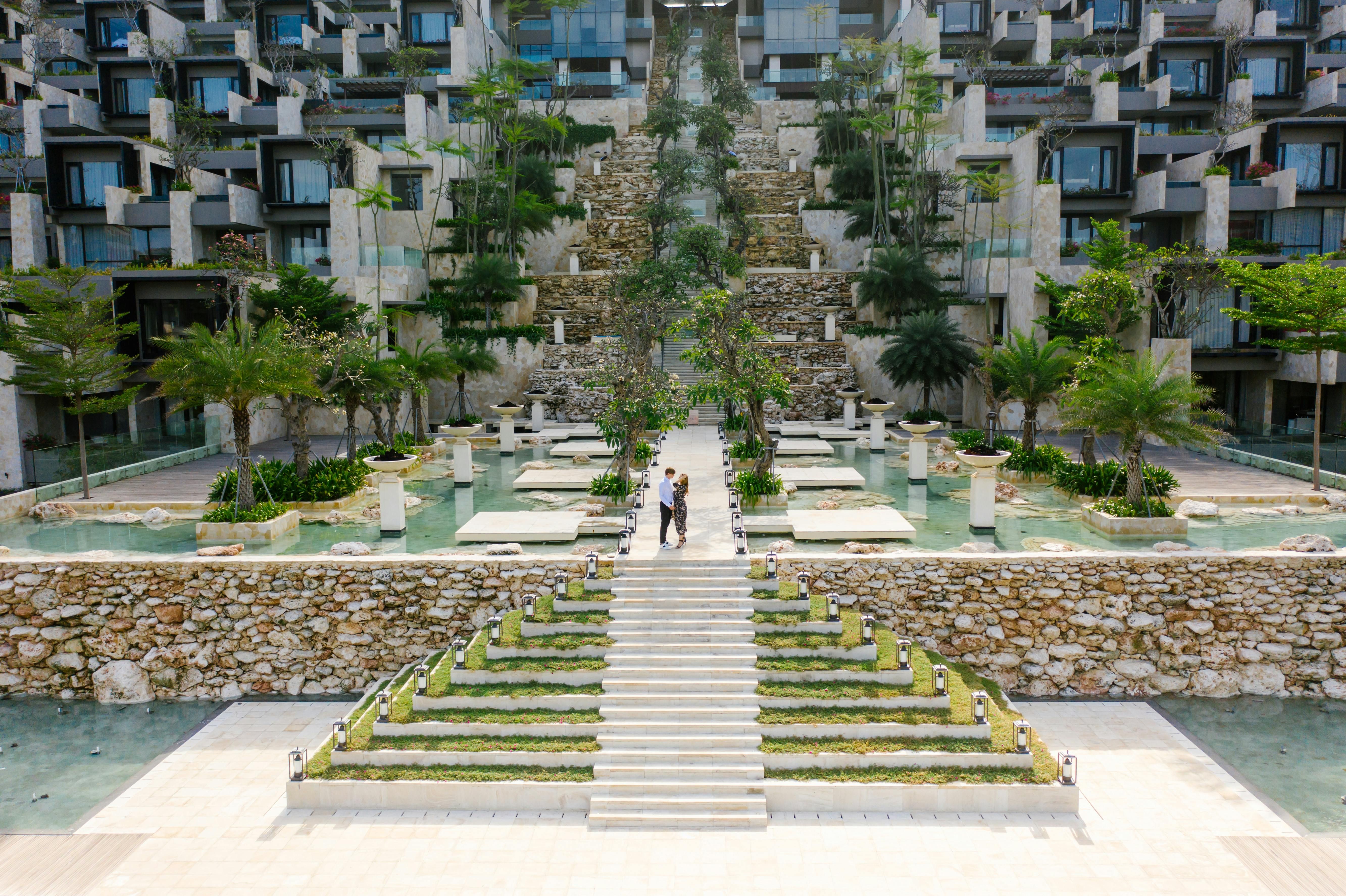 Bali — A couple walks through a modern resort with lush gardens and water features, showcasing luxurious architecture.