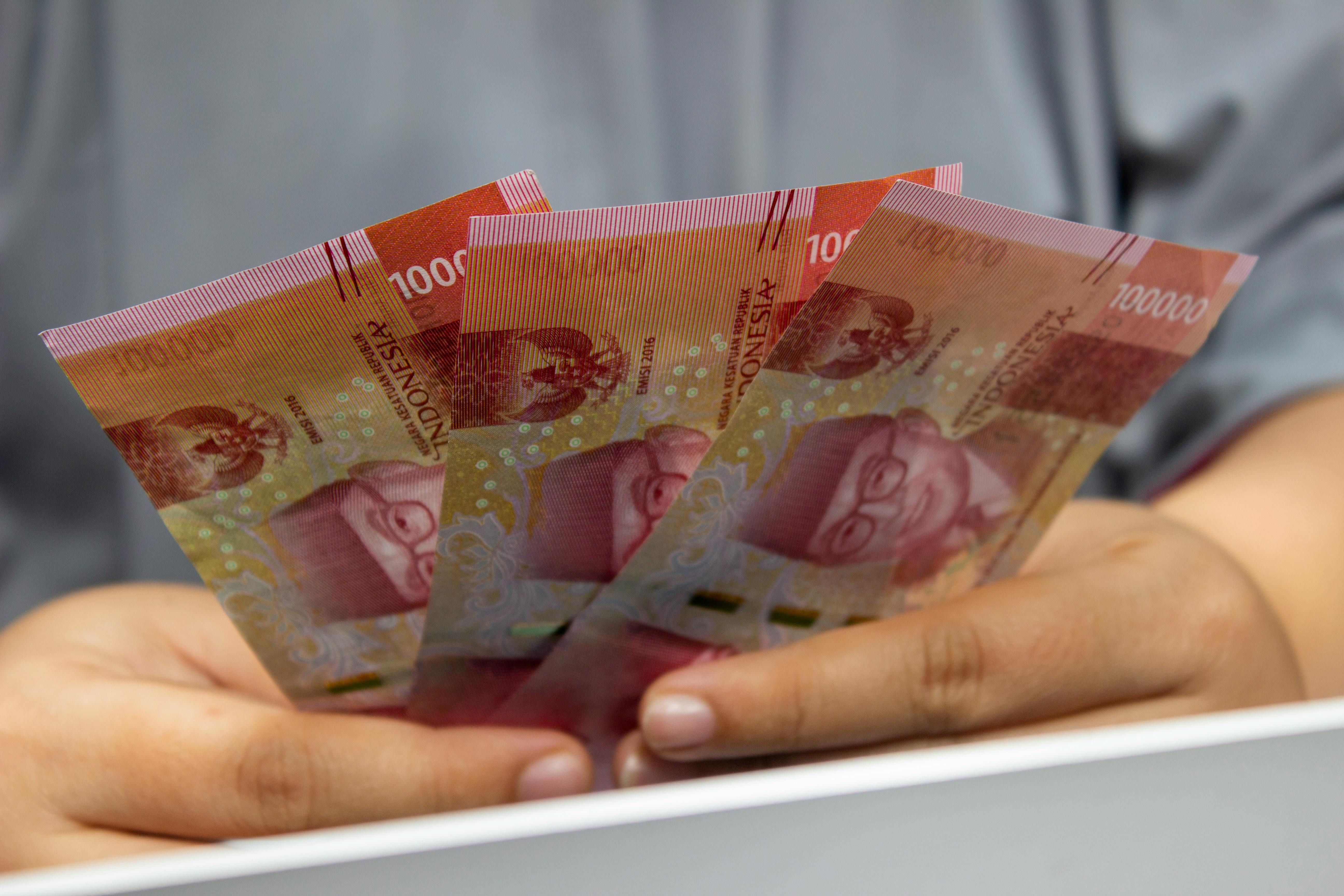 Bali — Hands holding multiple Indonesian Rupiah banknotes, showcasing currency details.