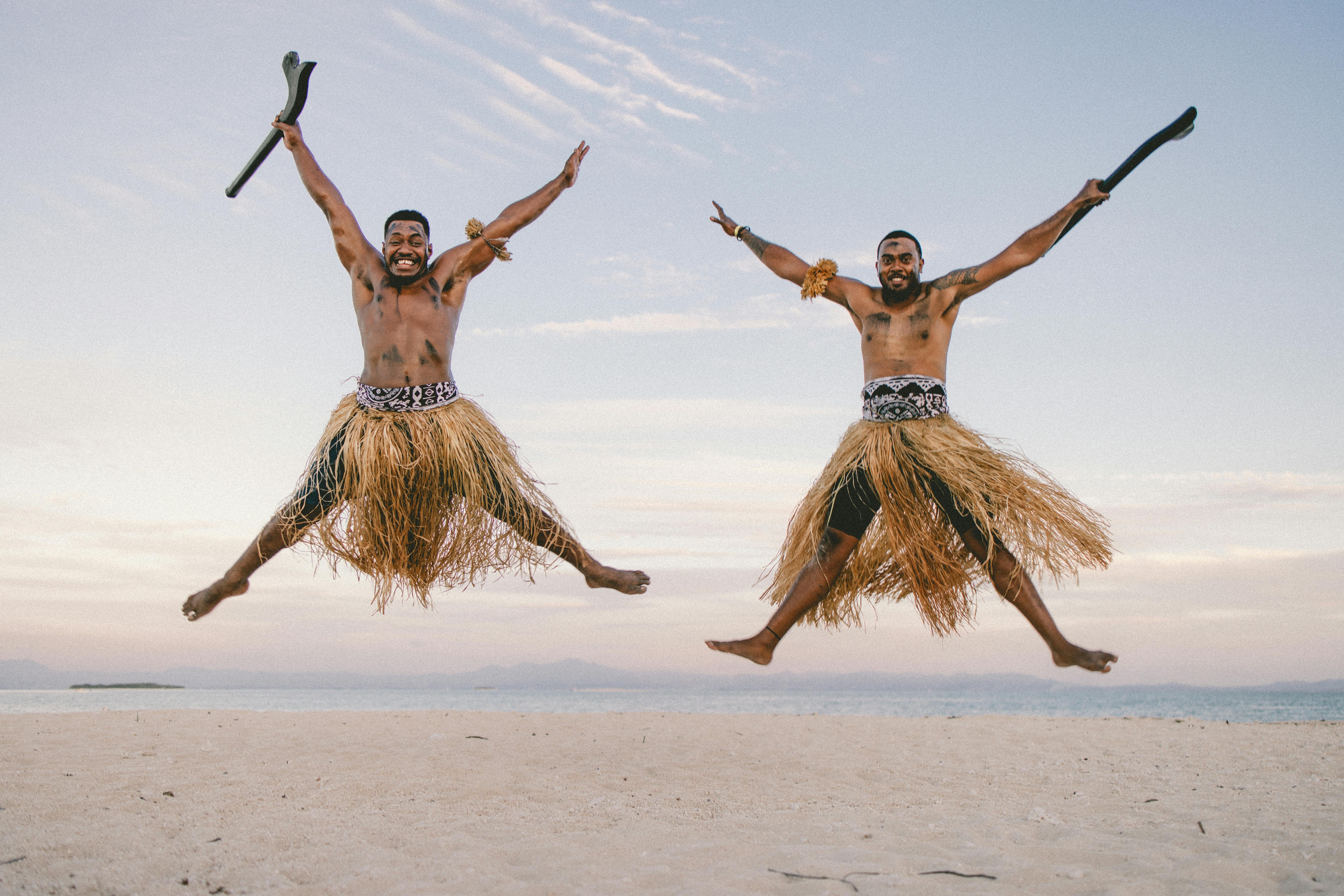 Fiji — Joyful Fijian men in traditional skirts leaping on a beach with the ocean in the background.