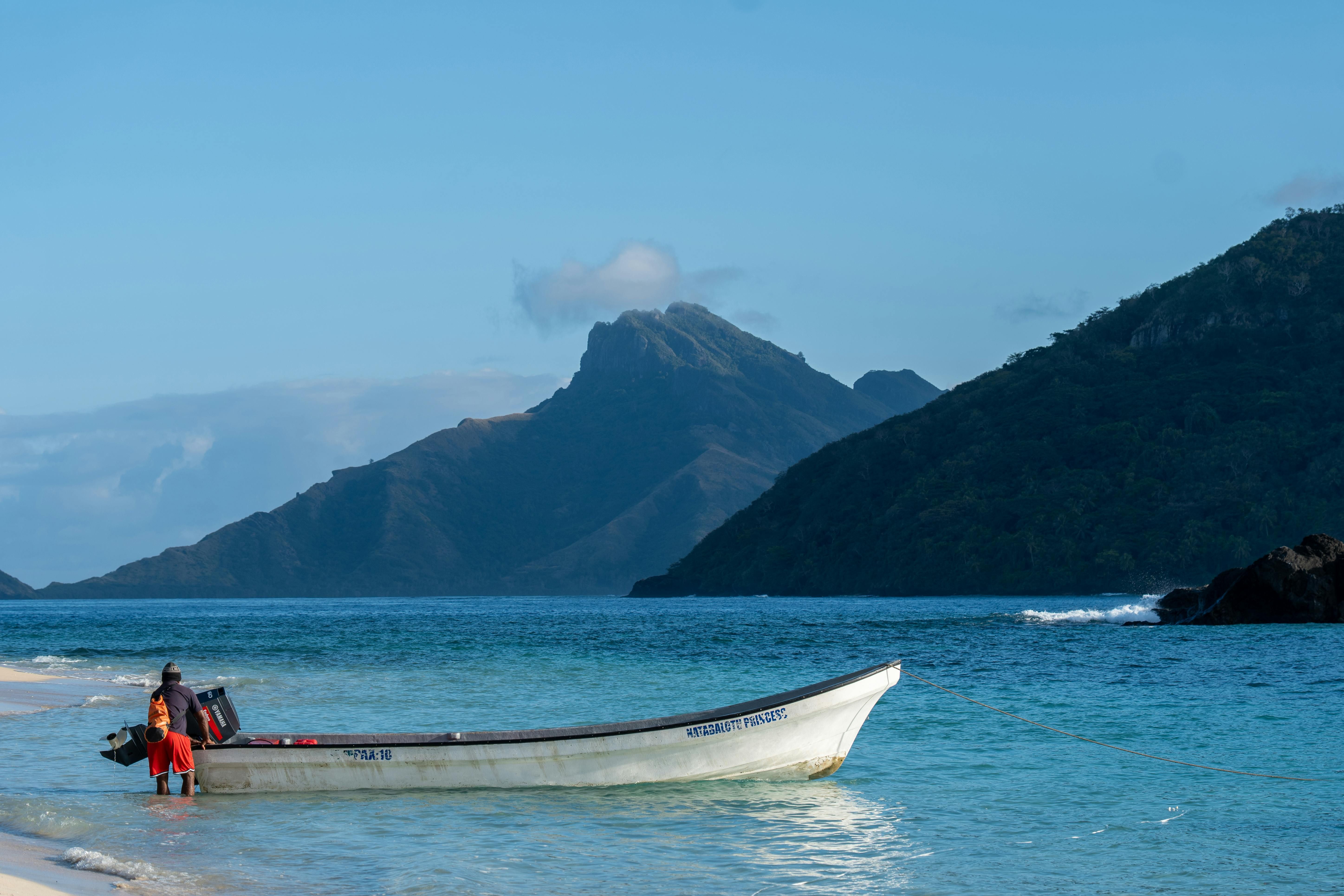 Fiji — A peaceful scene of a boat by a beach against Fiji's stunning mountainous backdrop.