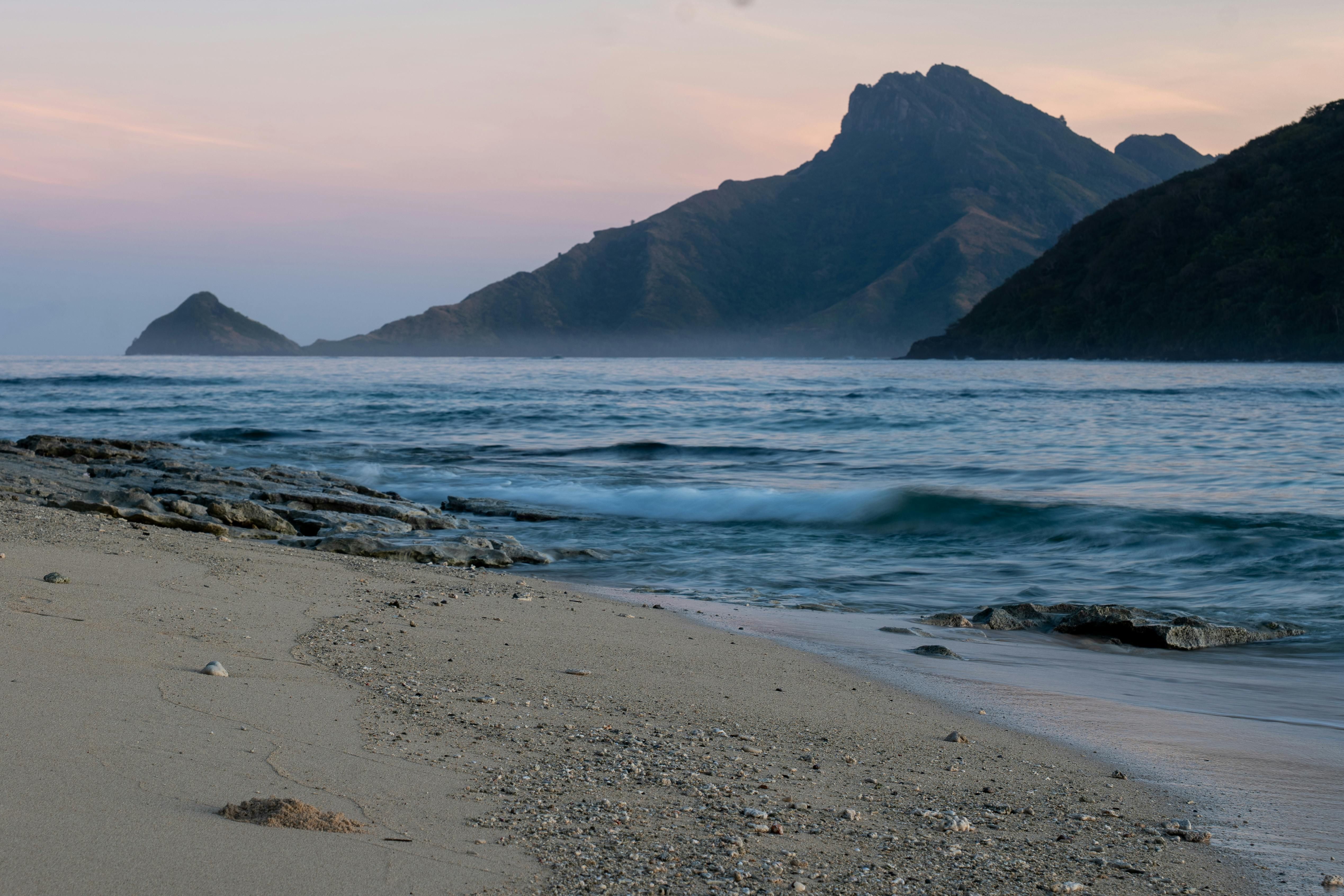 Fiji — Tranquil sunrise scene on a sandy beach with mountain views in the tropics.