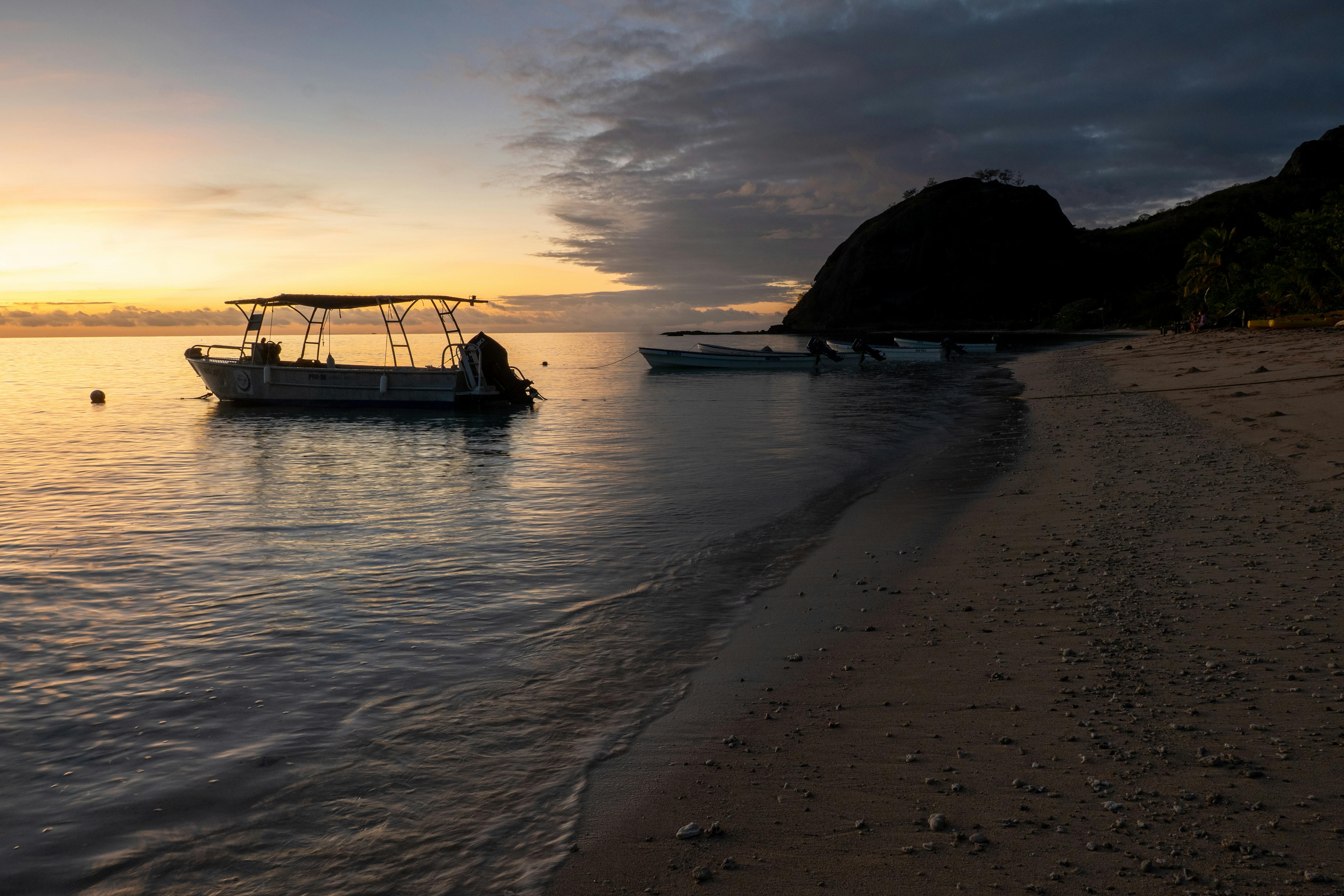 Fiji — Serene sunrise over a tranquil Fijian beach with a boat, capturing a peaceful island life.