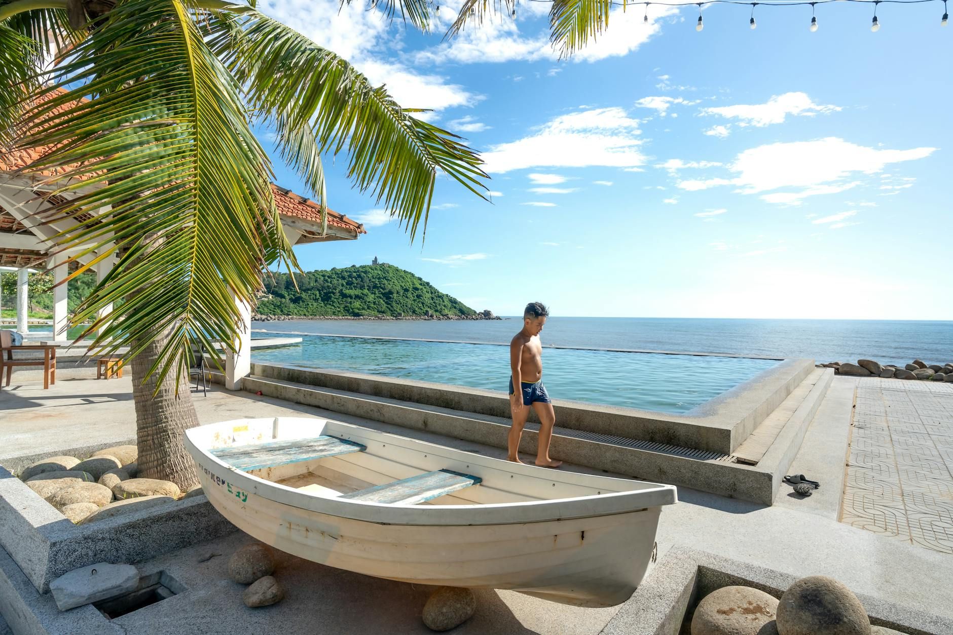 Man walking past boat beside infinity pool overlooking tropical ocean and island