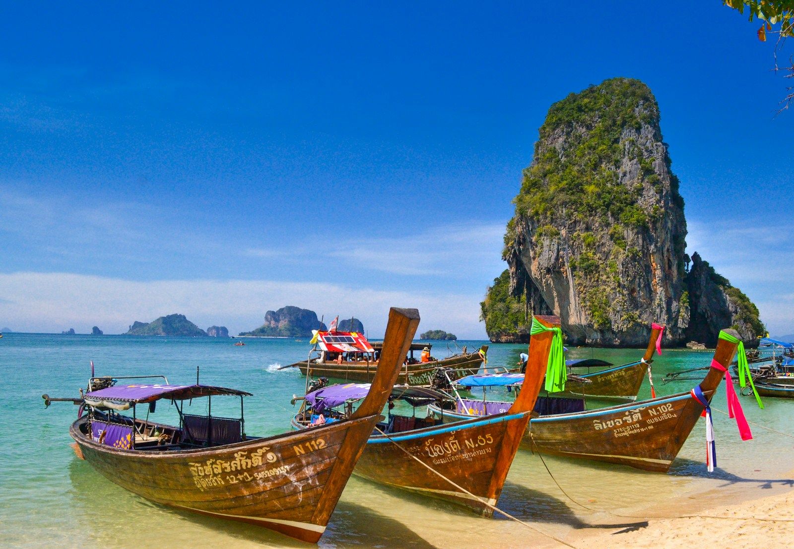 Traditional longtail boats on turquoise water with dramatic limestone karst cliffs backdrop in Thailand - Krabi — Via Resorts
