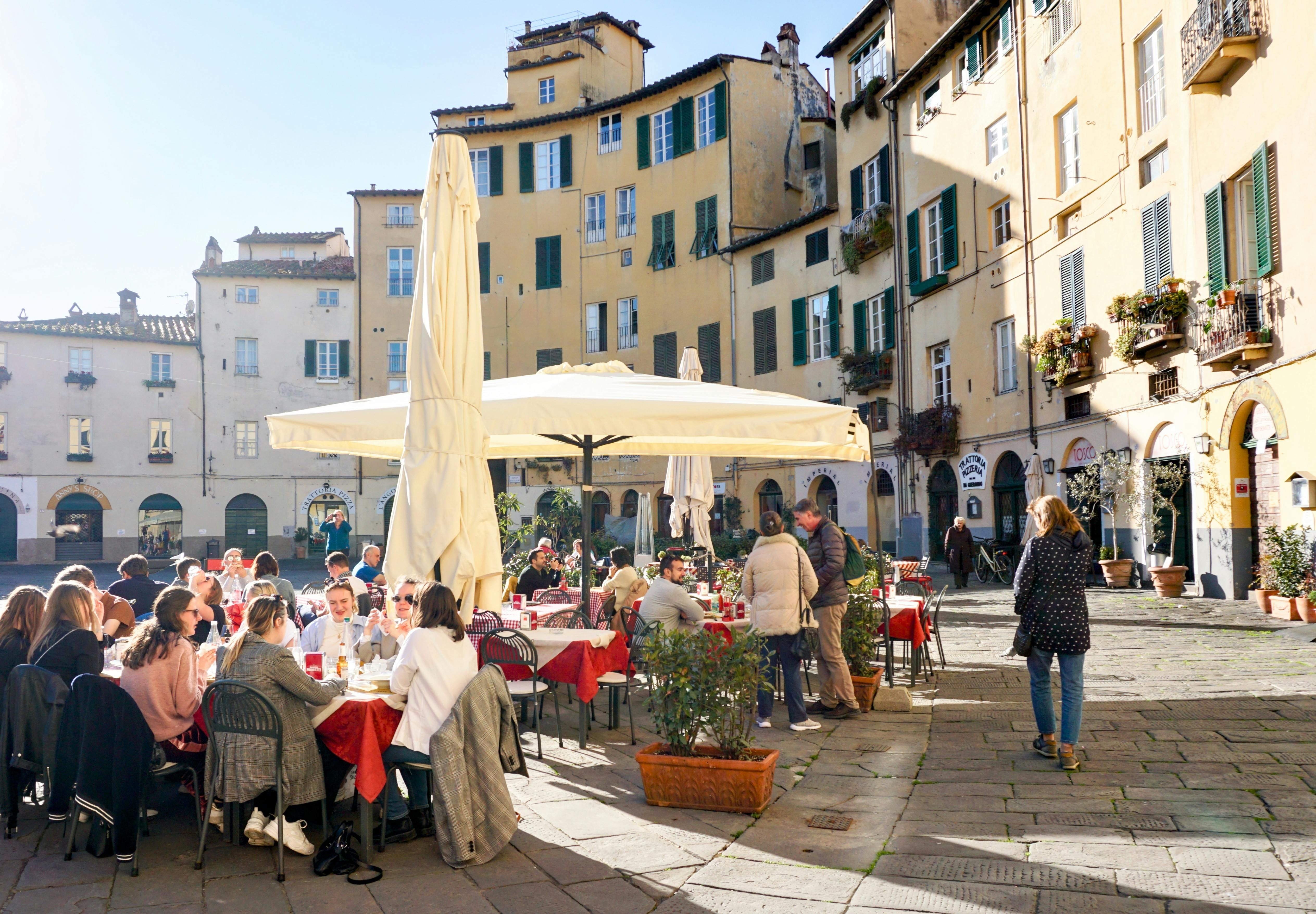 Italy — People enjoying an outdoor meal in Lucca's Piazza dell'Anfiteatro, Tuscany.