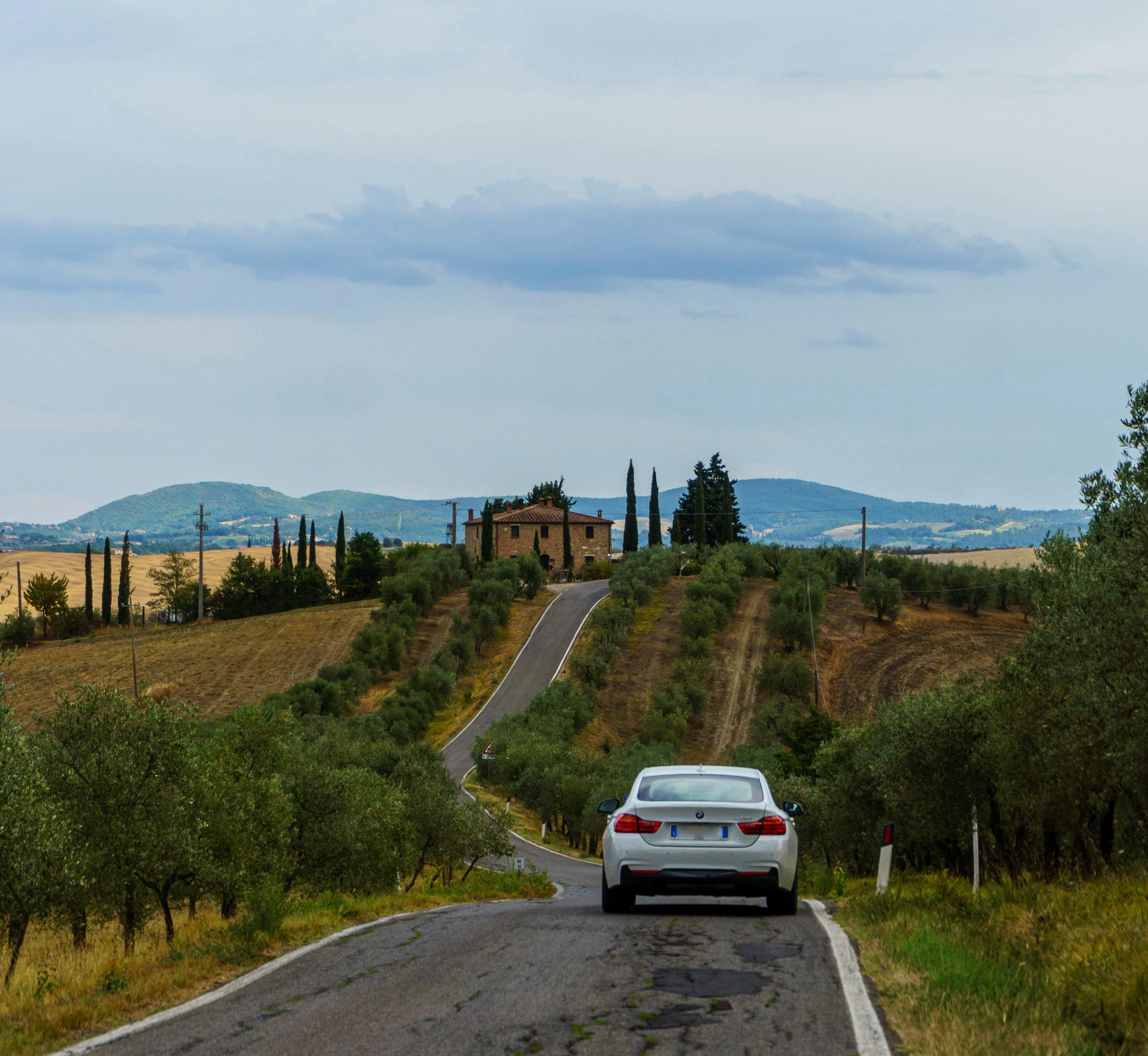 Italy — A car travels down a picturesque road in Tuscany, Italy, surrounded by olive groves and rolling hills.