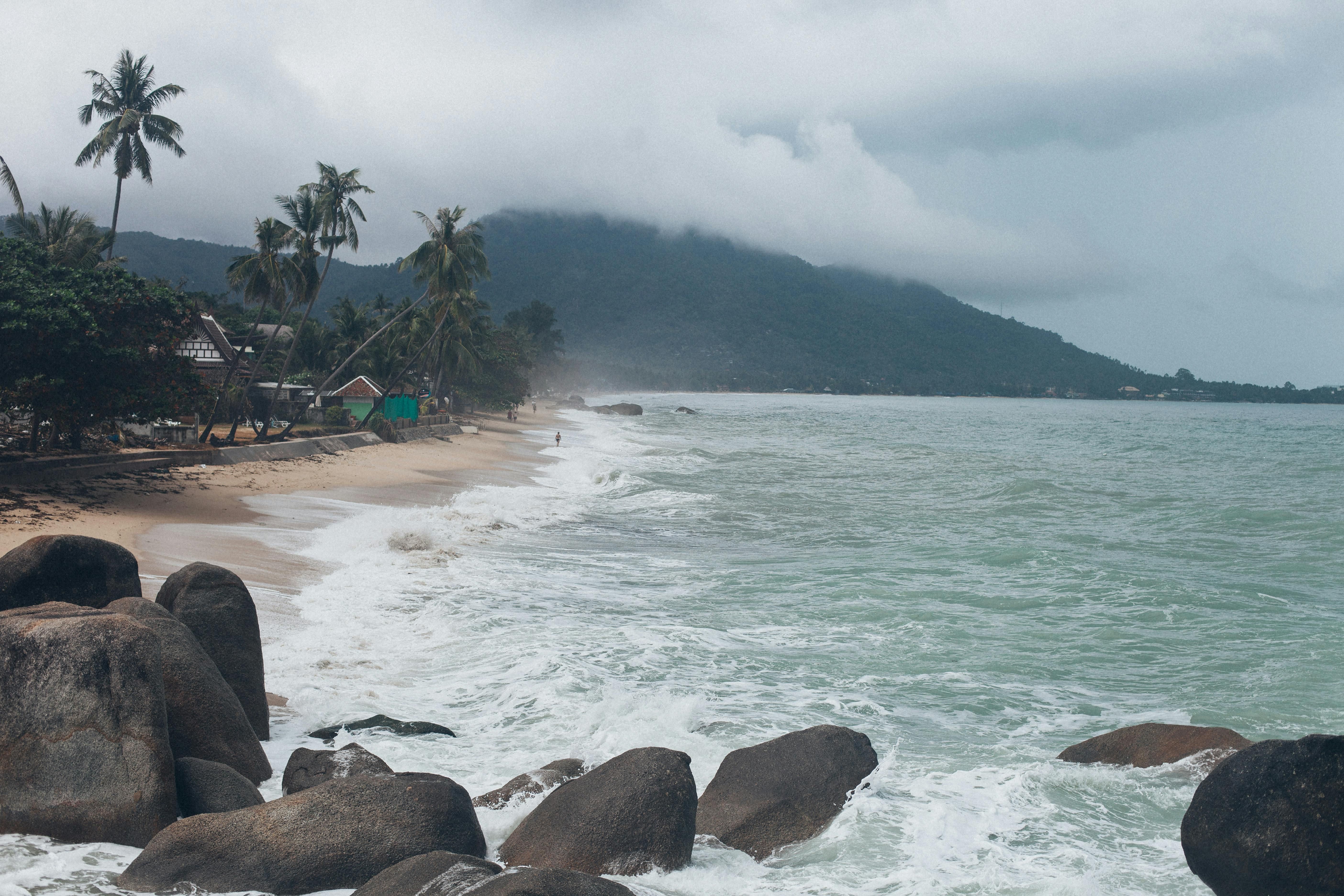 Koh Samui — Serene view of a tropical beach in Koh Samui, Thailand, with crashing waves and lush greenery.