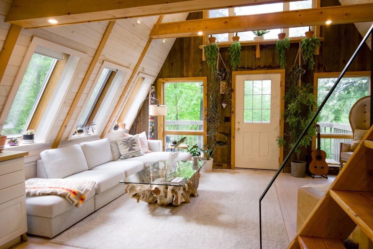 A-frame cabin interior with slanted windows, white sofa, plants, and rustic wooden decor in Unknown — Via Resorts