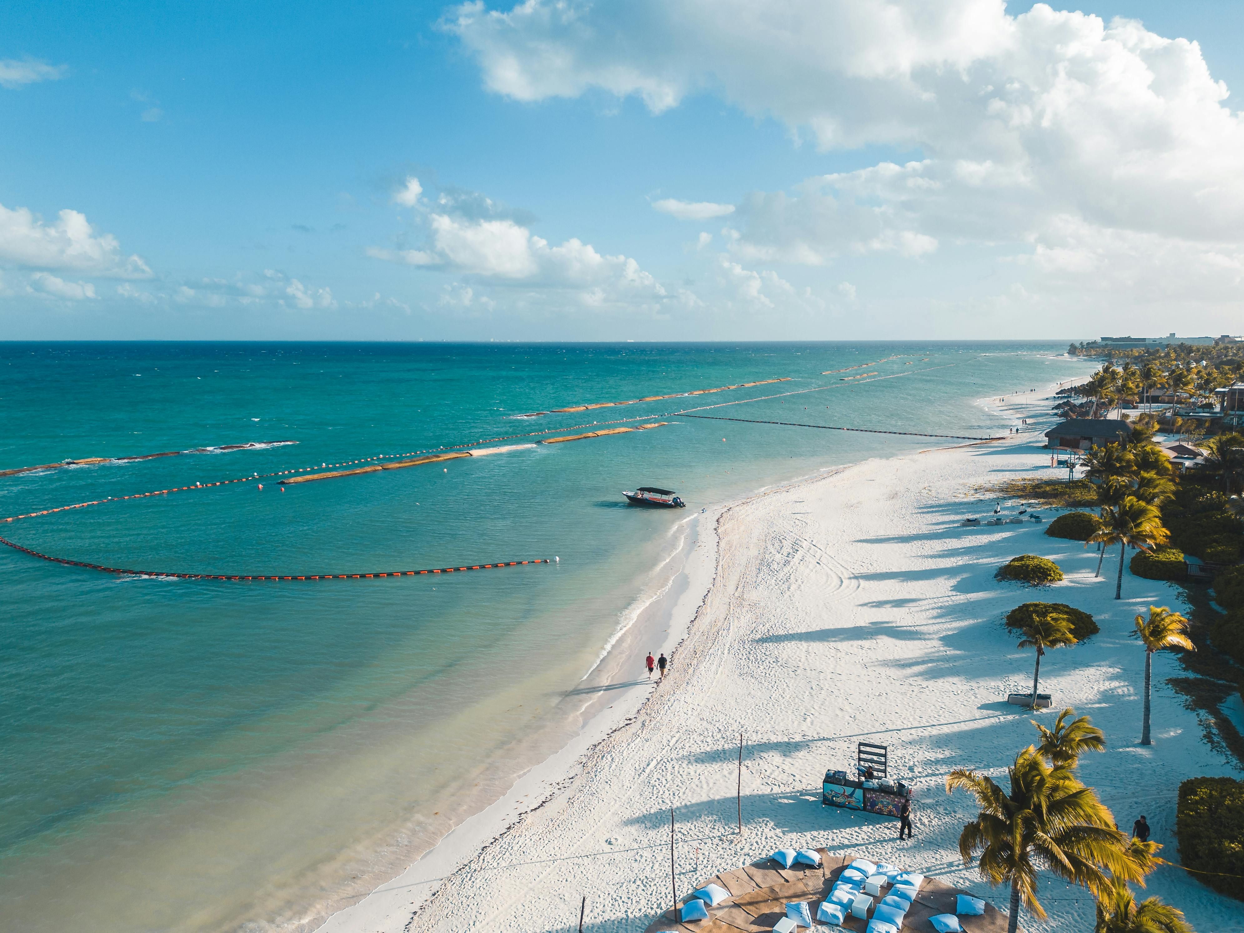 Mexico — A beautiful aerial view of Playa del Carmen's white sandy beach with clear blue waters and palm trees swaying in the tropical breeze.