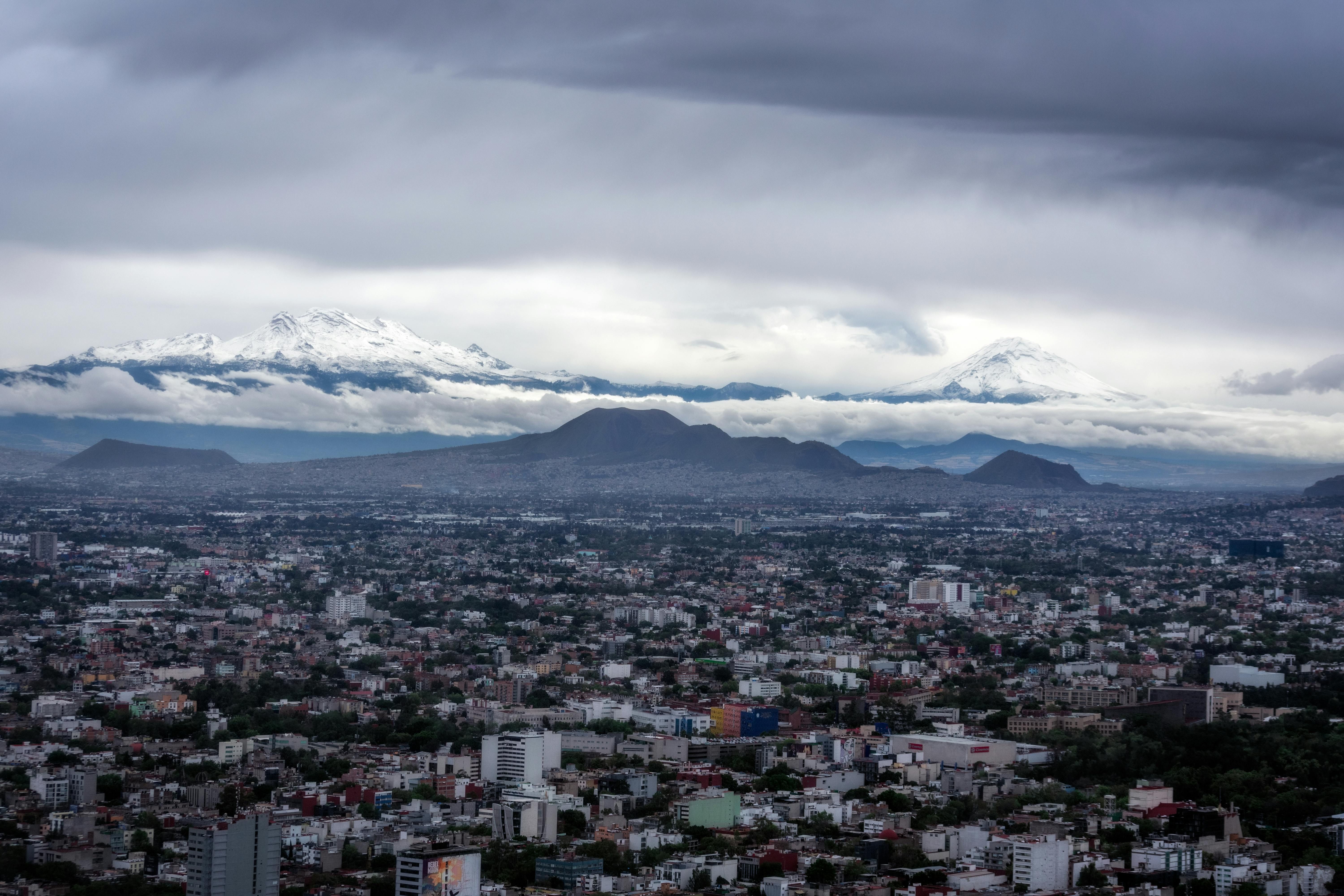 Mexico — Breathtaking aerial view of Mexico City with volcanic mountains under dramatic cloudy skies.