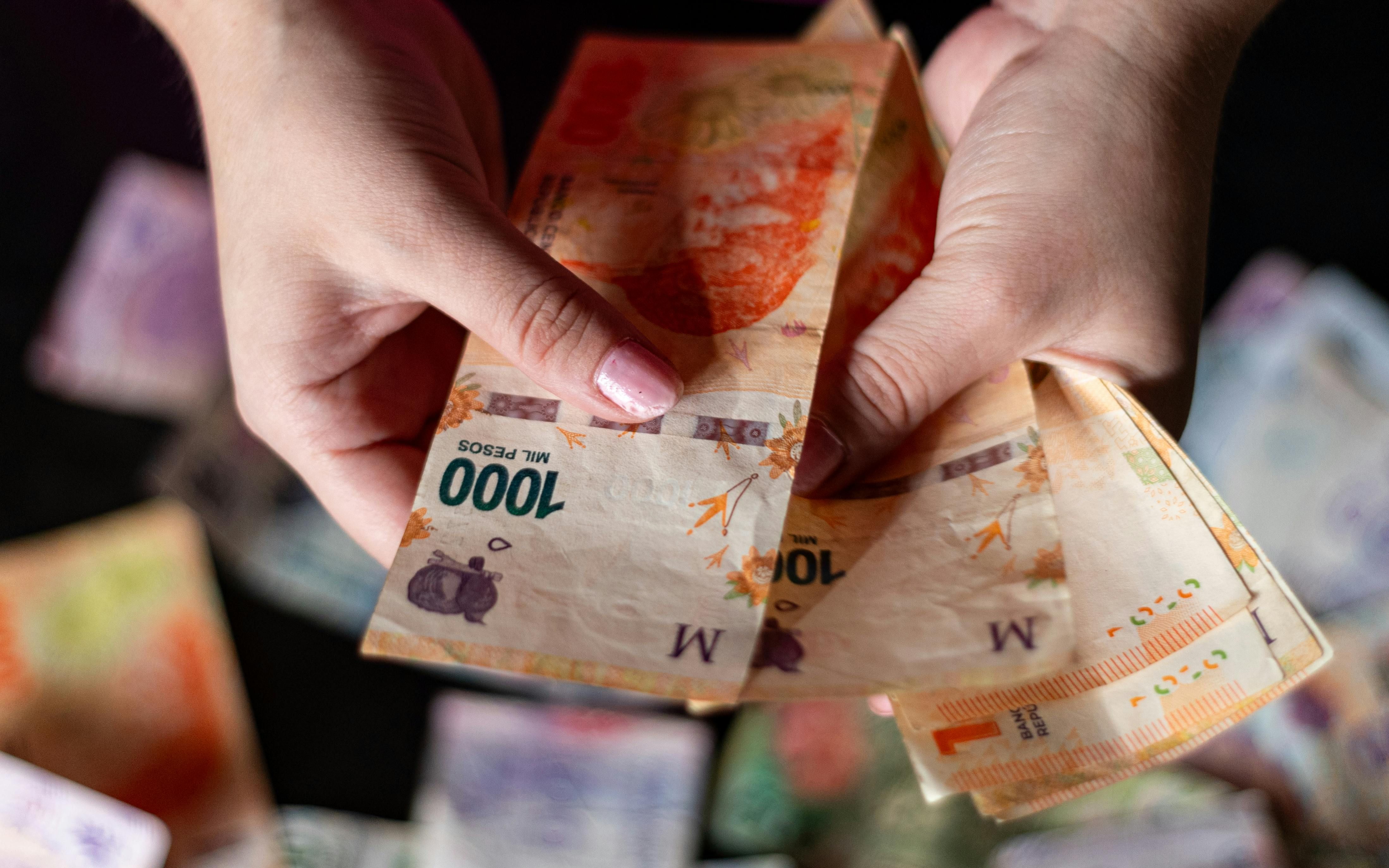 Mexico — Hands holding Argentine peso banknotes, showcasing currency details in Buenos Aires.