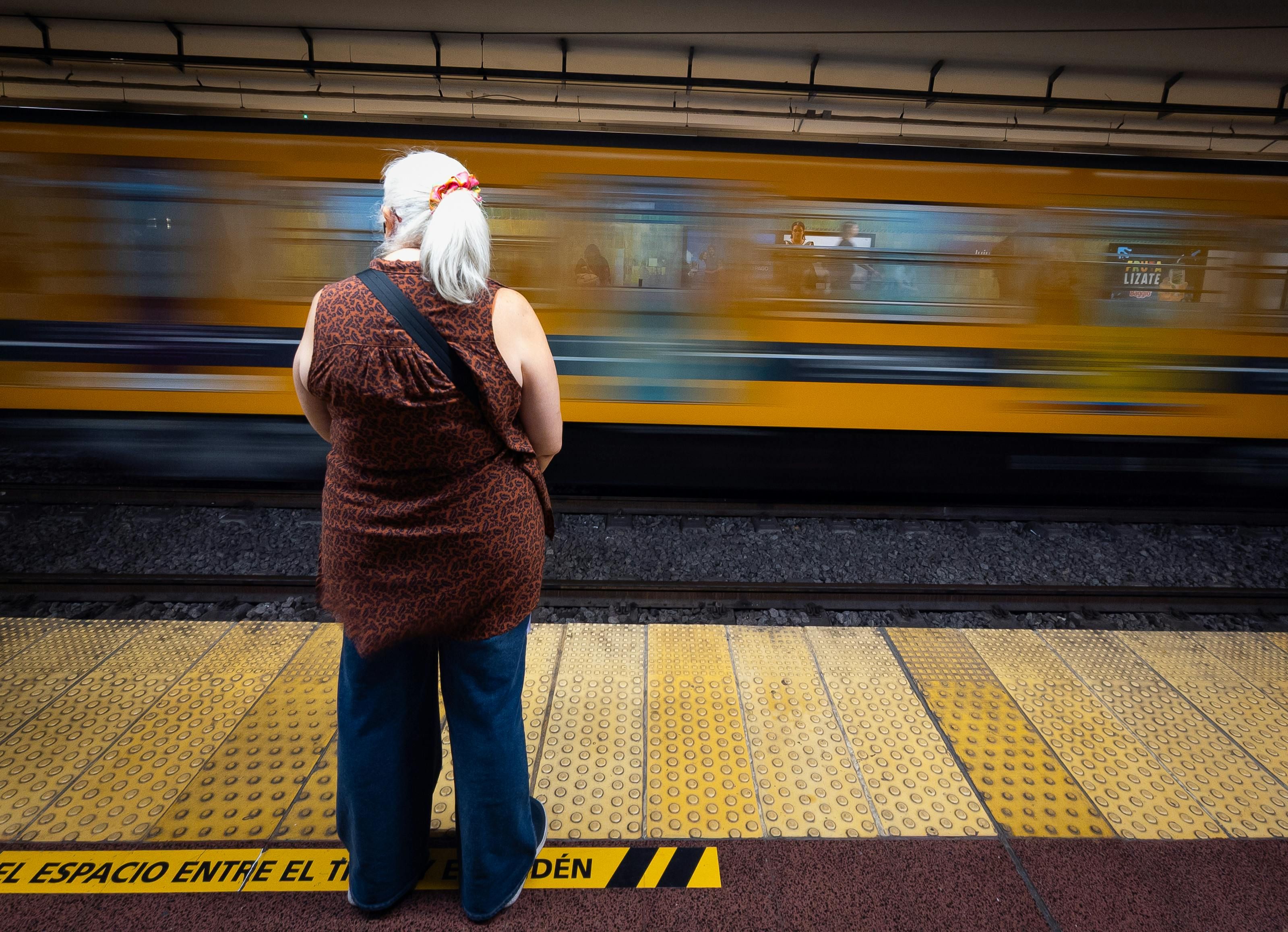 Mexico — Elderly woman waiting at platform as a train speeds by in an urban subway station.