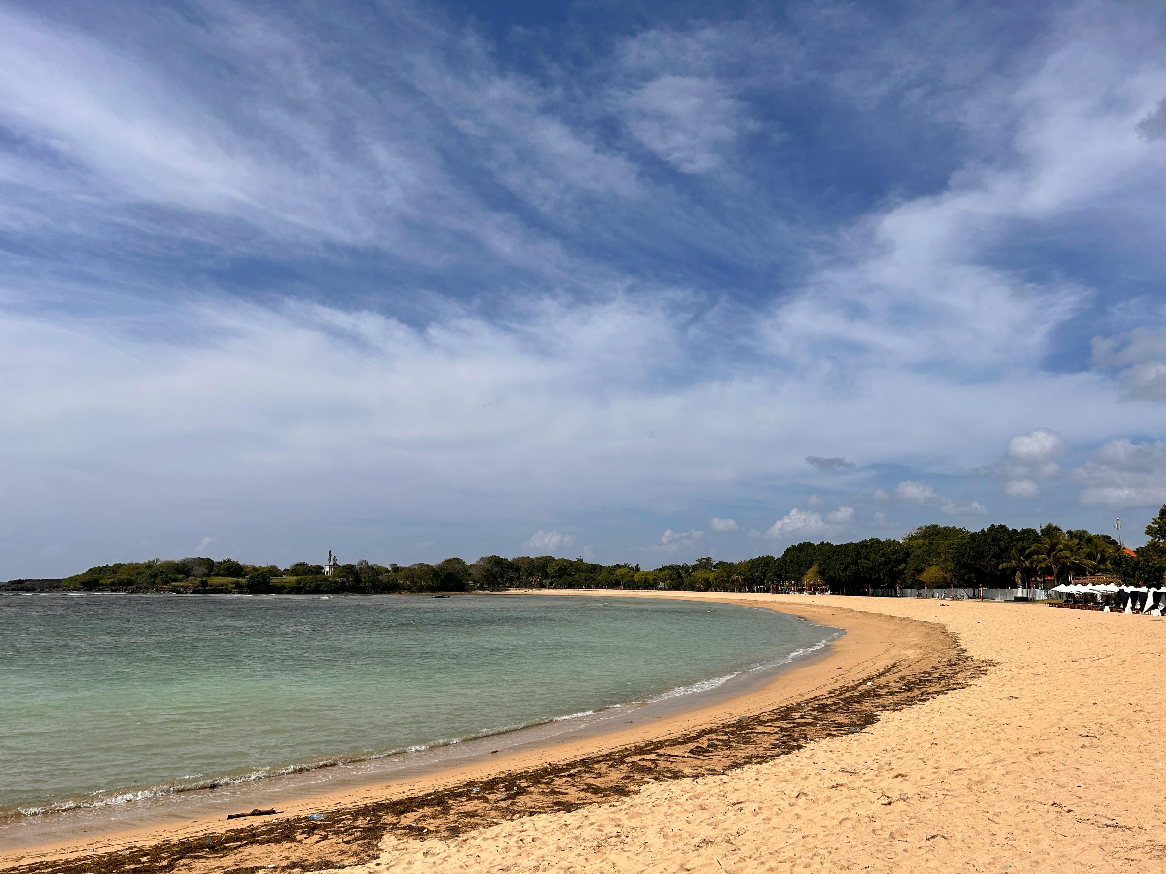 Nusa Dua — Serene sandy beach curved along a calm sea under a bright, clear sky.