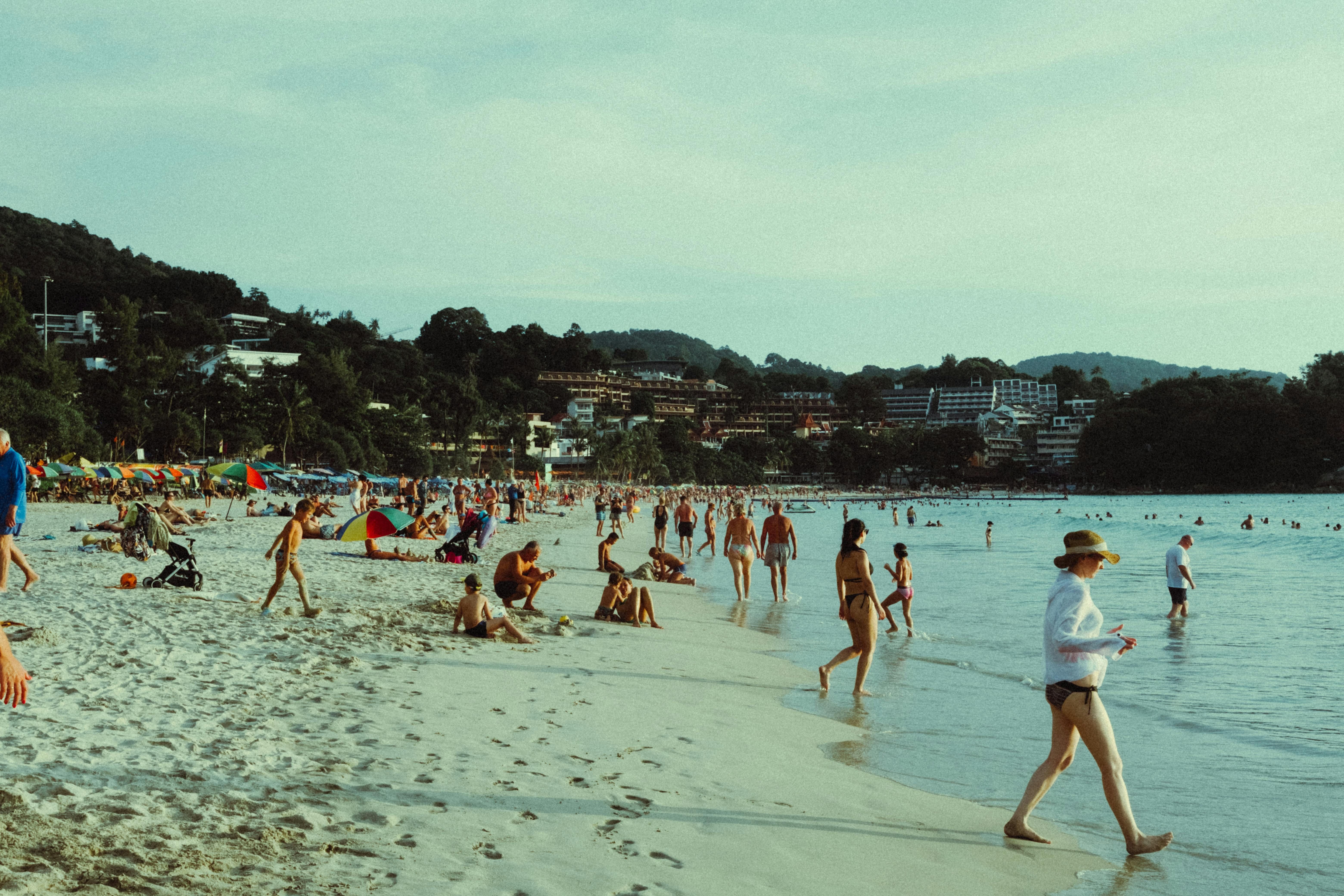 Thailand — People enjoying a vibrant day at a tropical beach, with umbrellas and lush greenery.