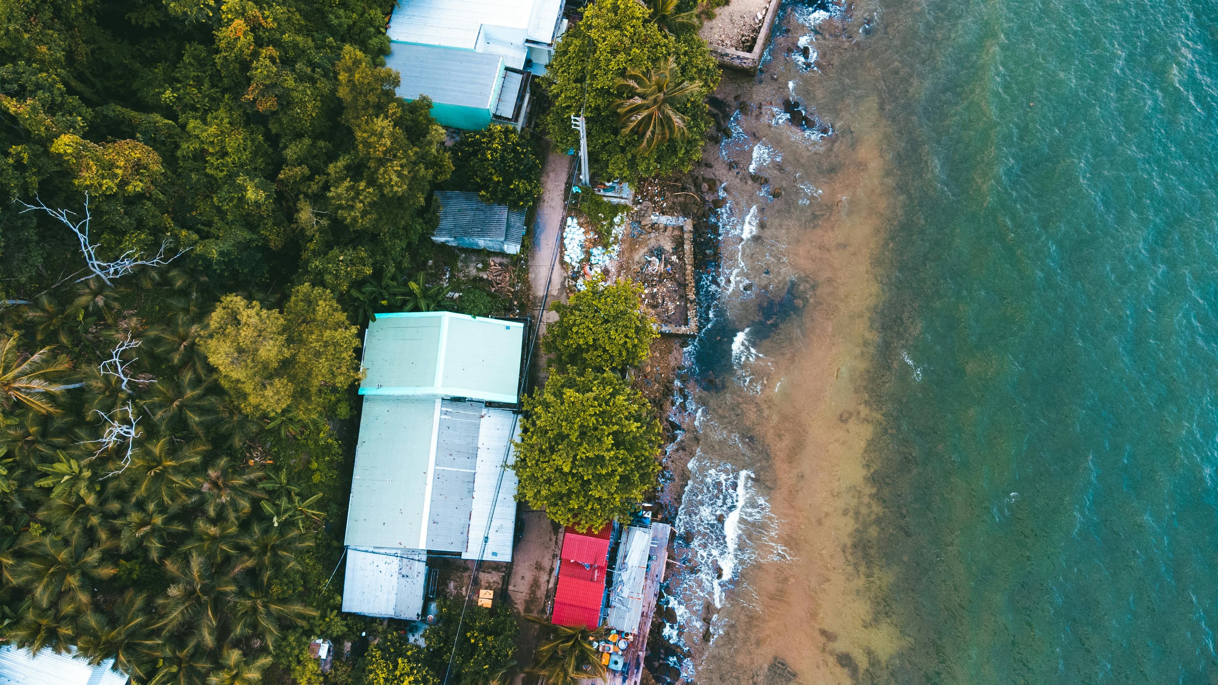 Thailand — Aerial view of houses and lush greenery along a sandy coastline with clear blue waters.
