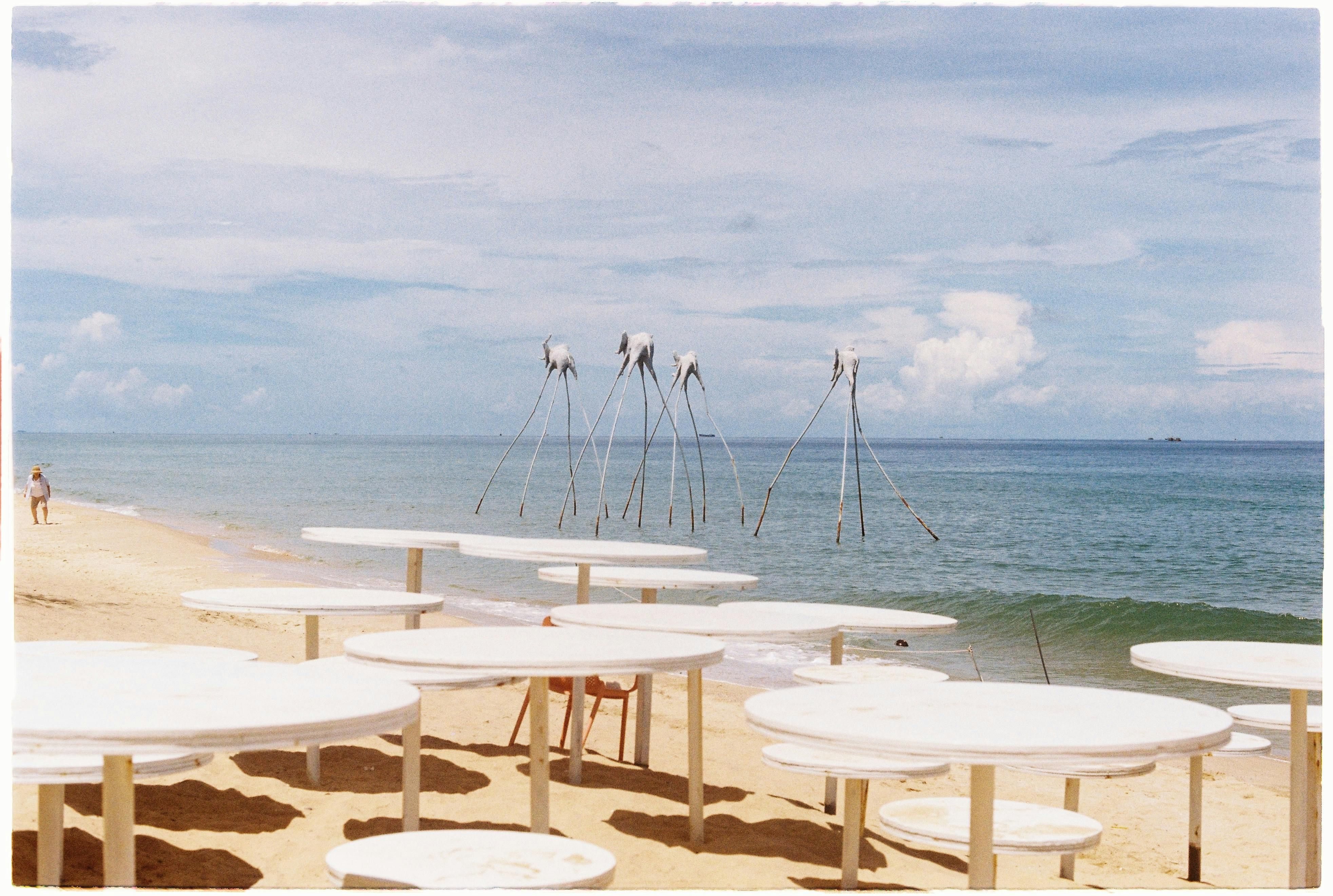 Vietnam — Explore a tranquil beach scene with white tables and unusual sculptures by the sea.