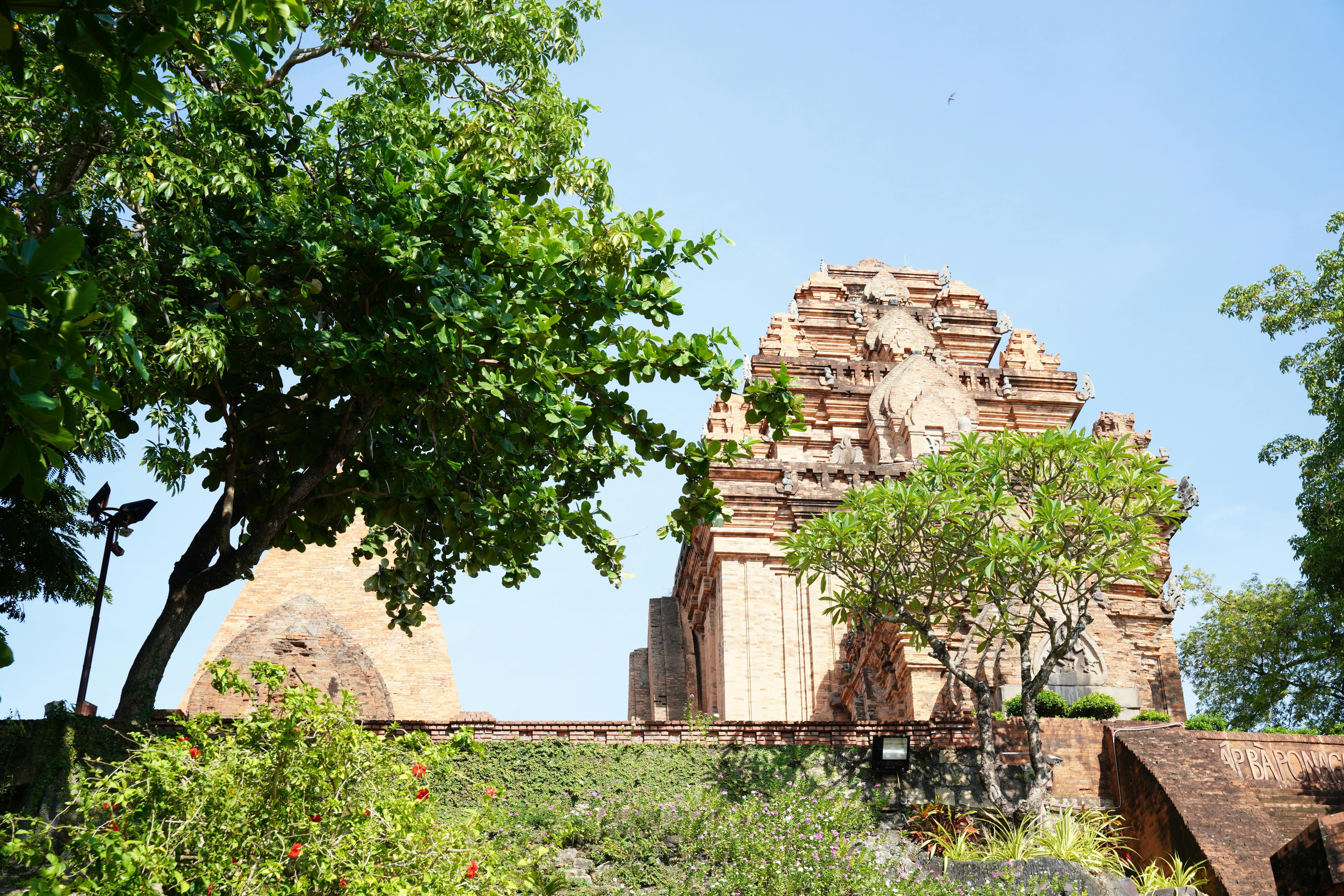 Vietnam — A historic red brick temple amidst vibrant greenery under a clear blue sky showcasing Vietnamese architecture.